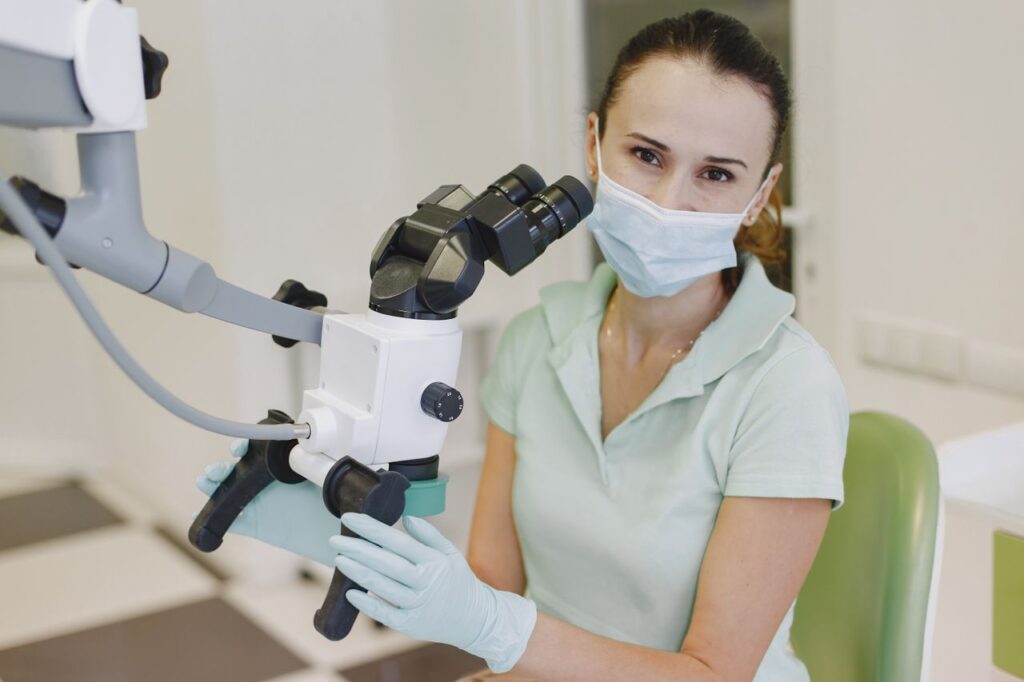 Female scientist wearing mask examines samples using microscope in lab.